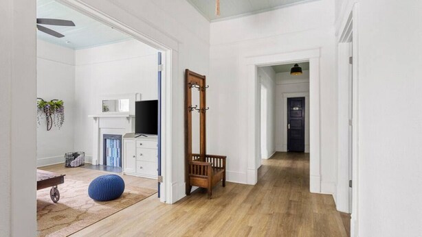 A spacious hallway with wooden flooring, white walls, and a large mirror. There is a wooden bench and a blue ball on the floor.
