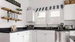 A modern kitchen with white cabinets, a black countertop, a stainless steel dishwasher, and a coffee maker.