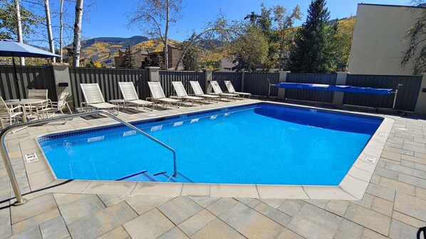 Una piscina rectangular con borde de azulejos, rodeada de sillas de descanso y un área de estar techada.