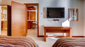 A hotel room with a bed, a TV mounted on the wall, a wooden desk, and a bathroom visible through an open door. - Westwind 101 2bd, 2BA Diamond Condo in Lionshead Village (Vail)