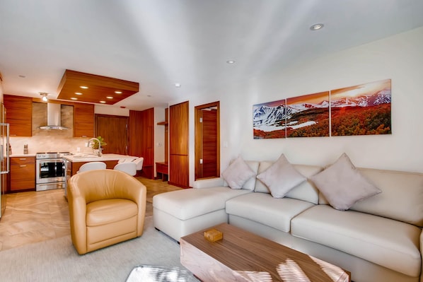 A modern living room with a sofa, a coffee table, and a dining area with a kitchen in the background.