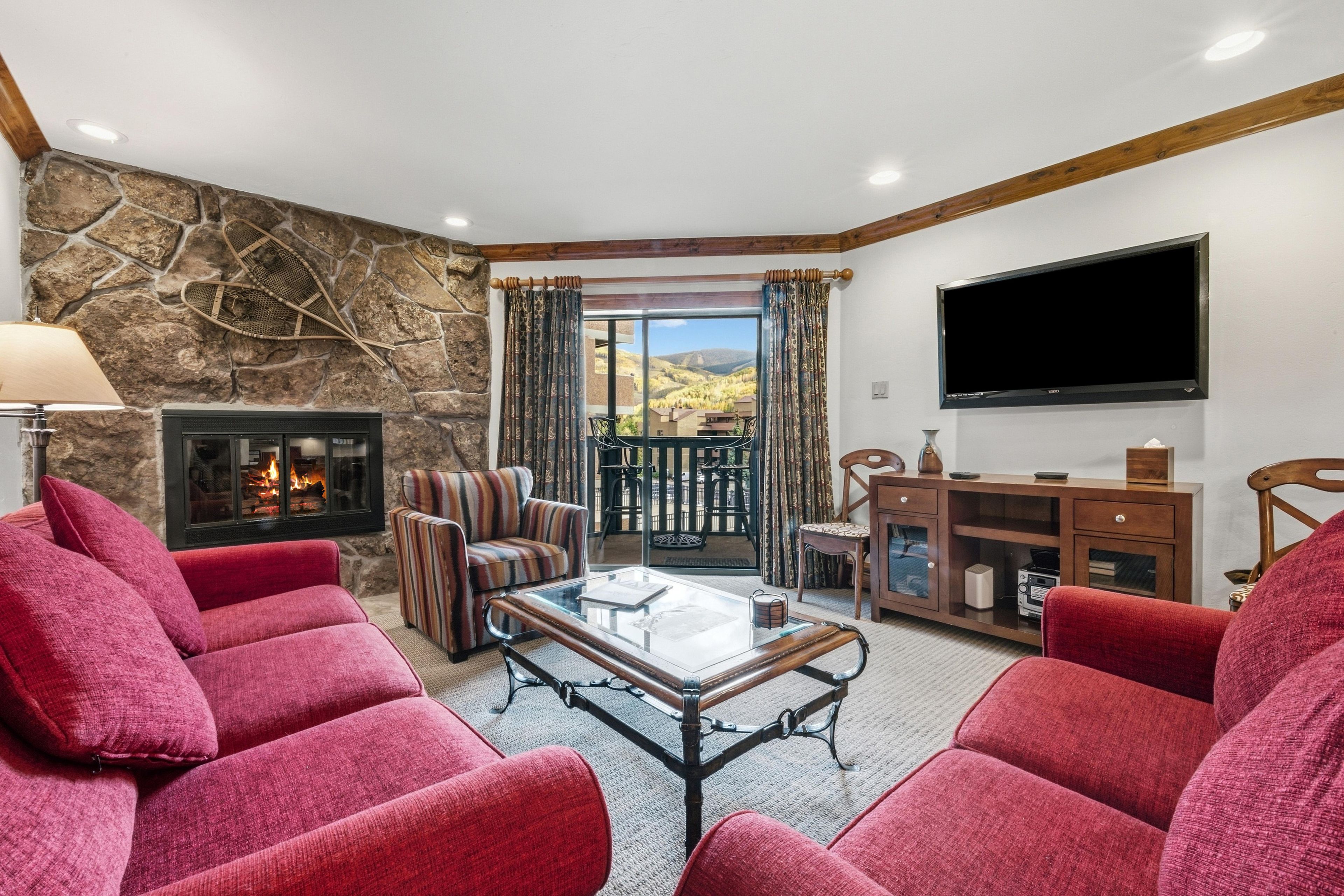Una sala de estar con una pared de piedra, una chimenea, un televisor y vistas al exterior.