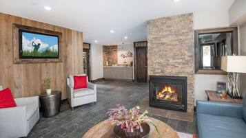 Una sala de estar moderna con chimenea, un televisor montado en una pared de madera y una zona de cocina al fondo.