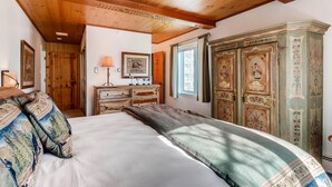 Un dormitorio con techo de madera, una cama con almohadas estampadas, un aparador y un mueble de almacenamiento con motivos florales.