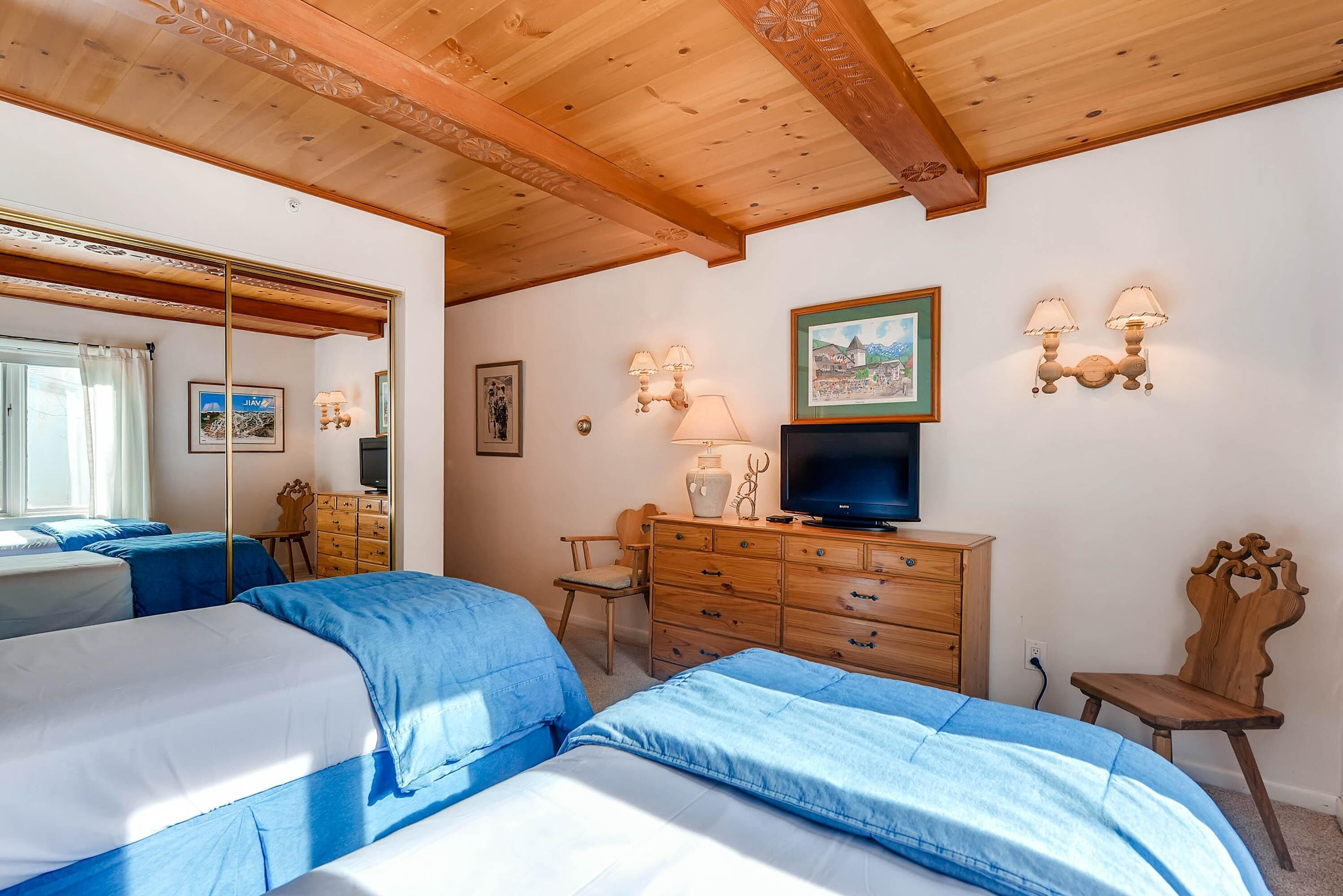 A bedroom with two beds, a wooden dresser, a television, wall-mounted lamps, and a mirror.