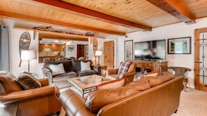 Amplia sala de estar con sofás de cuero, techo de madera y televisor.