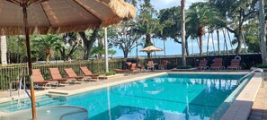 A swimming pool with lounge chairs and umbrellas, surrounded by palm trees and a fence. - Tropical Resort & Marina on Lake Beresford (DeLand)