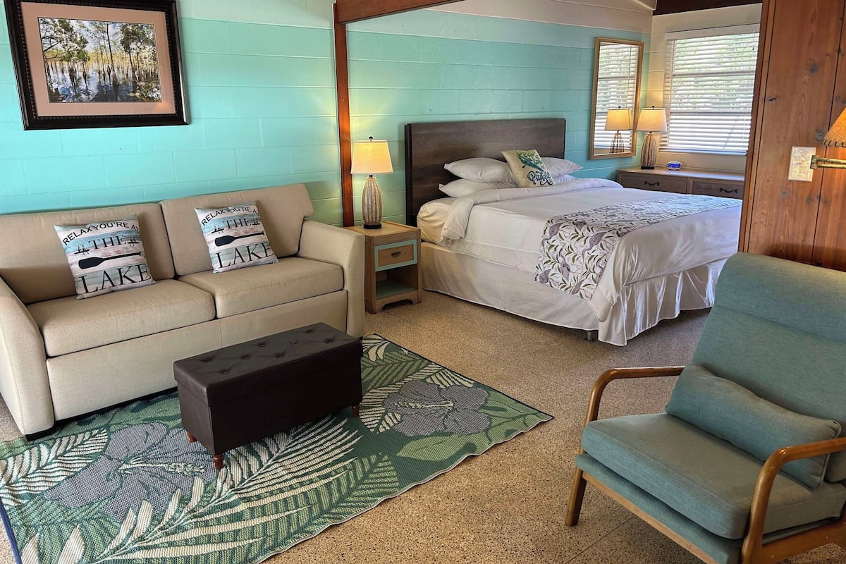 A room with a bed, a sofa, a chair, and a nightstand with a lamp.