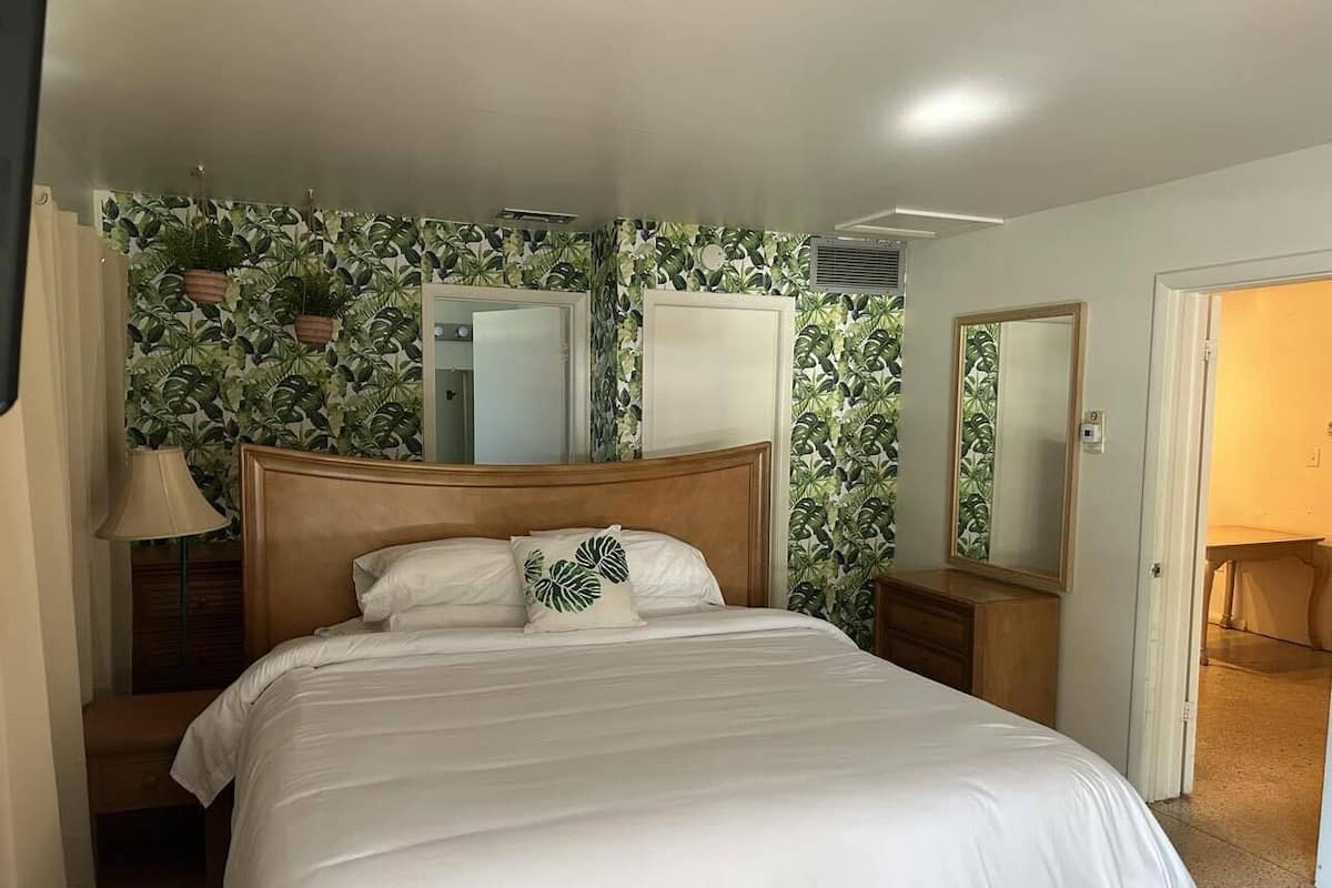 A bedroom with a large bed, wooden headboard, two bedside tables, a nightstand, a lamp, and a mirror.