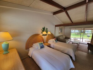 A hotel room with two beds, a wooden headboard, a small table with a lamp, and a view of the outdoors through large windows. - Tropical Resort & Marina on Lake Beresford (DeLand)