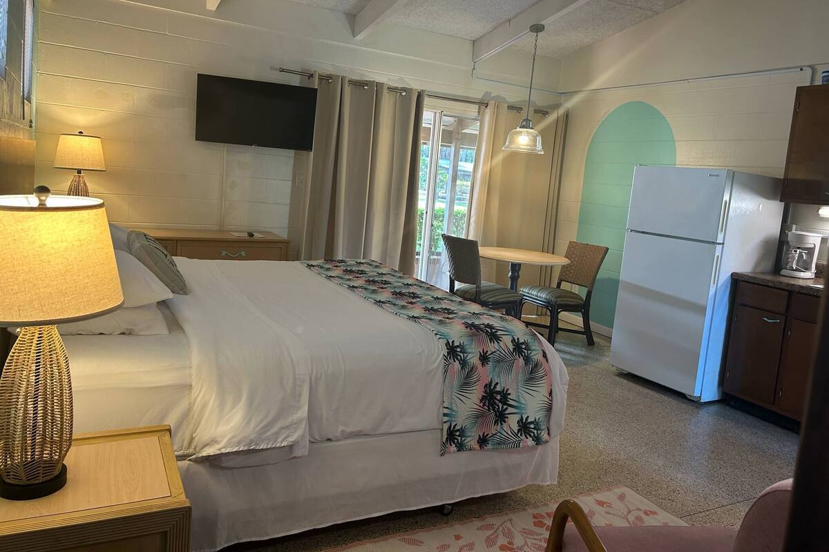 A hotel room with a bed, a desk, a chair, a television, a refrigerator, and a window with curtains.