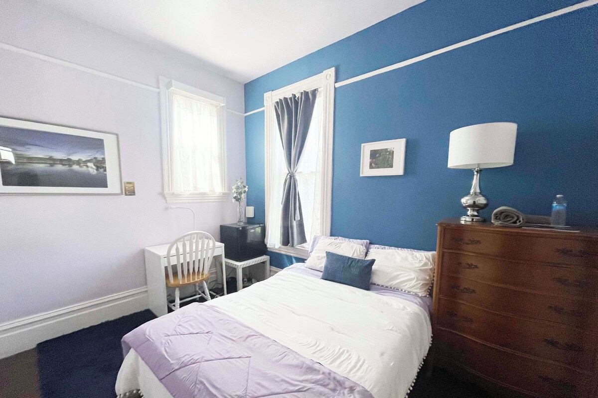 A bedroom with a bed, a desk, a chair, a dresser, and a window with curtains.