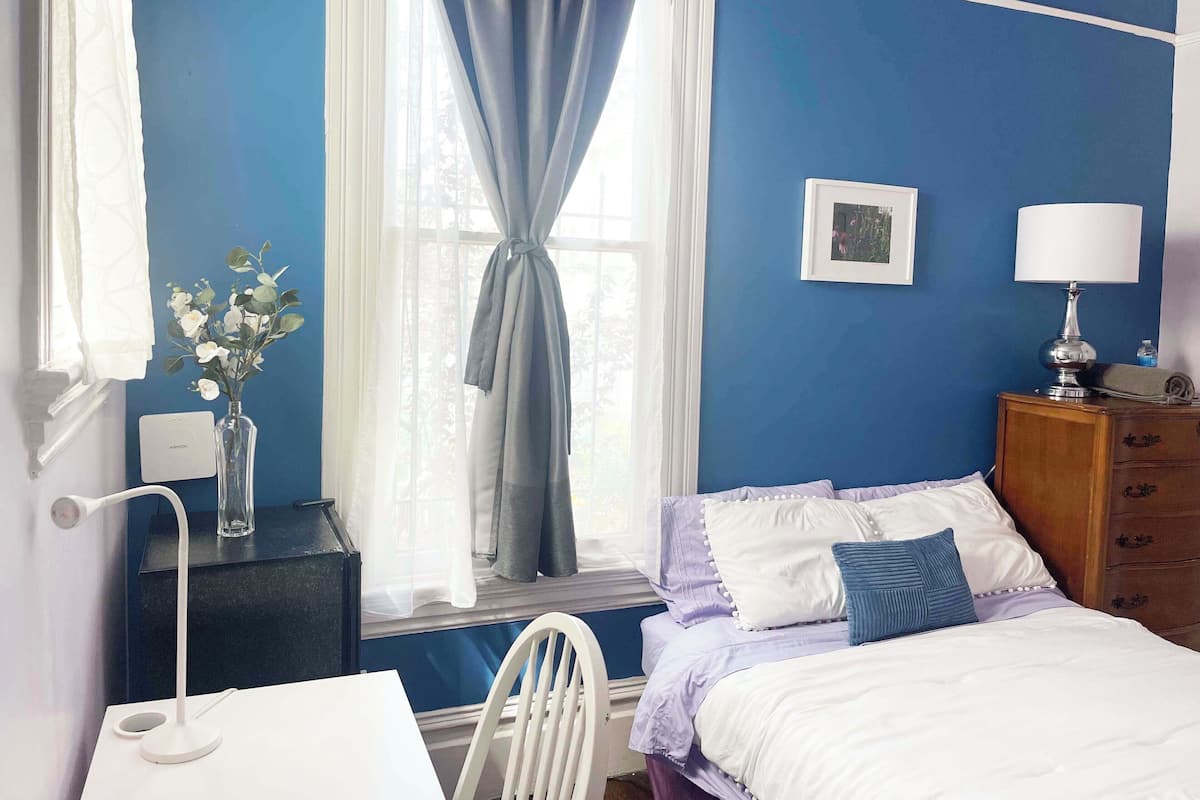 Une chambre à coucher avec un lit, une table de chevet, une lampe et une fenêtre avec des rideaux.