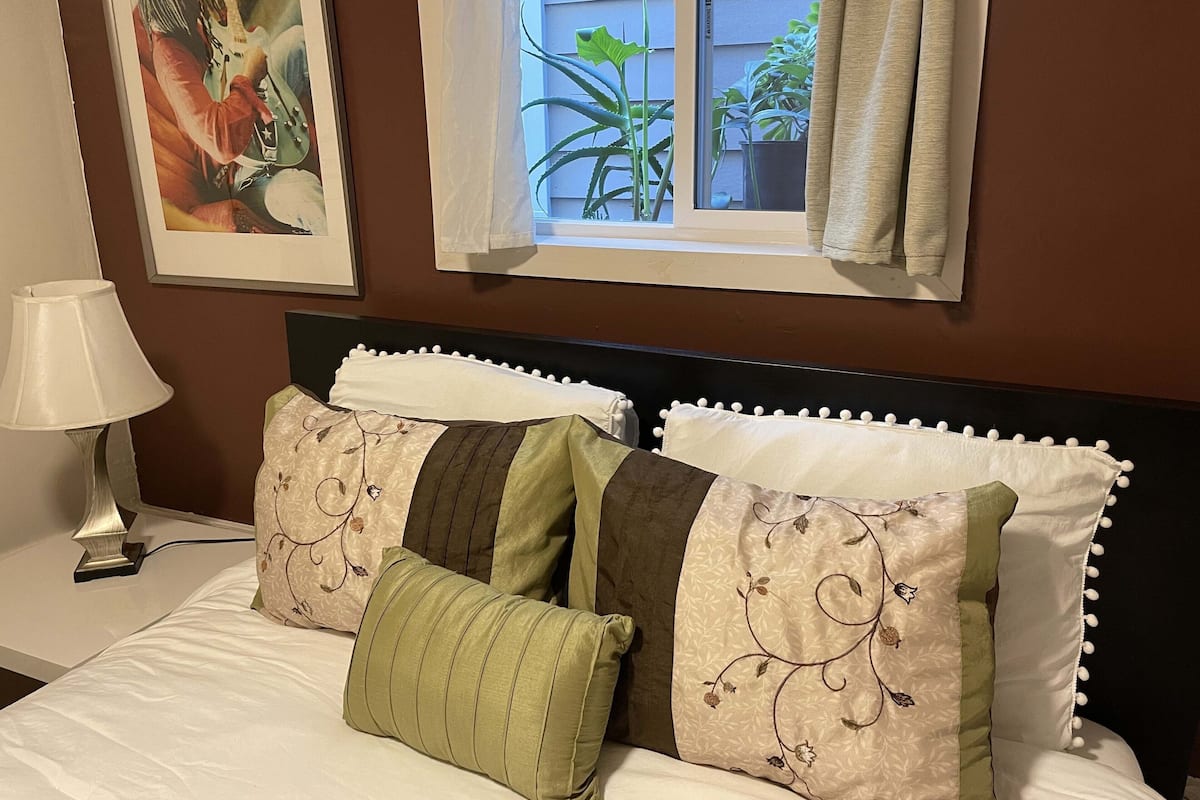Un lit bien fait, agrémenté de coussins décoratifs, d’une lampe de chevet et d’un tableau encadré au mur.