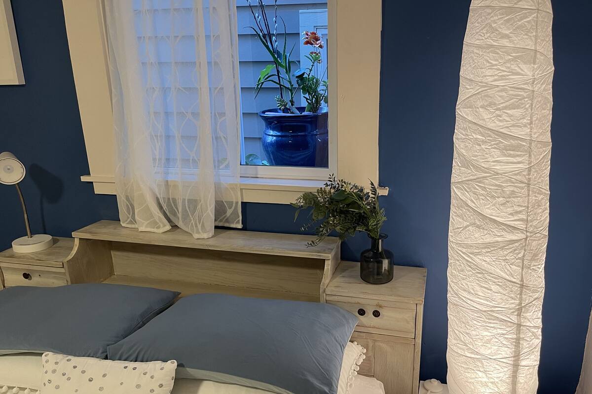 Une chambre à coucher avec un lit, des tables de chevet, une fenêtre donnant sur l’extérieur et un rideau.