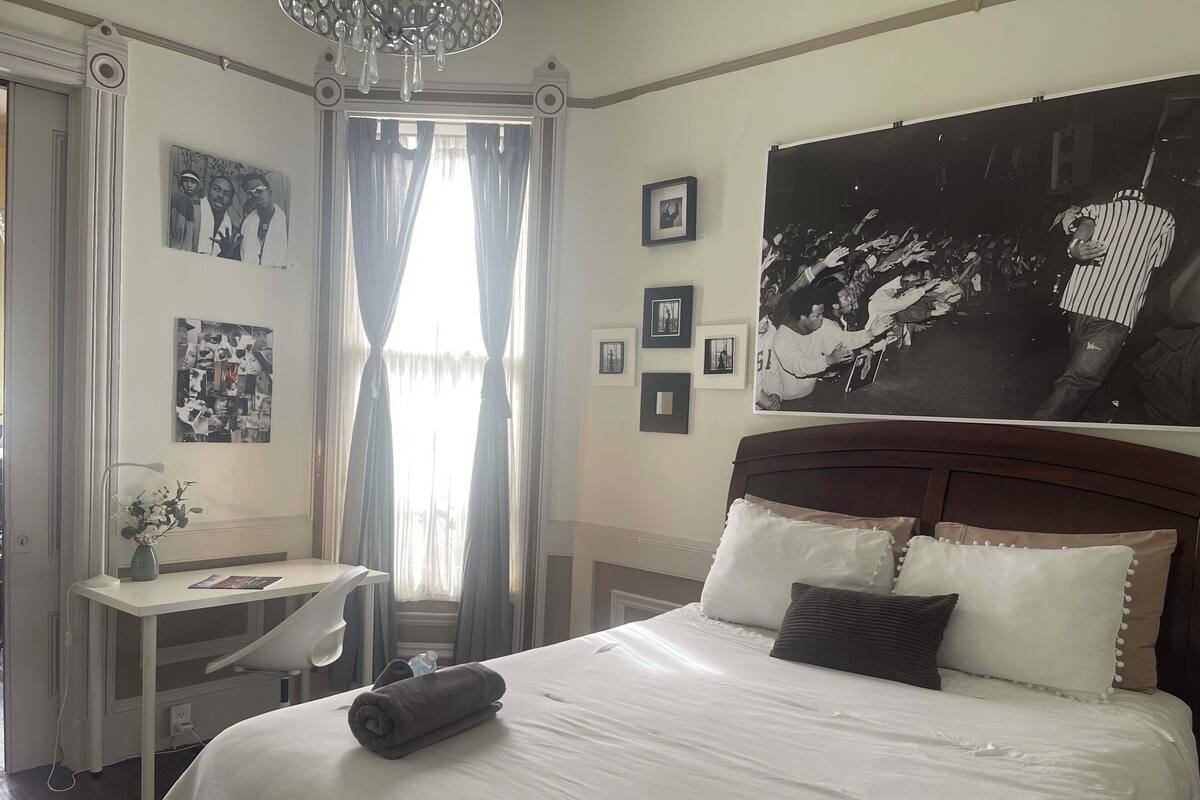 Une chambre d’hôtel comprenant un lit, un bureau, une chaise, une fenêtre avec des rideaux et des éléments de décoration murale.