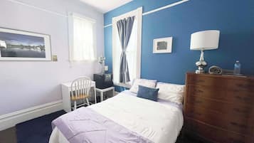 Une chambre à coucher comprenant un lit, un bureau, une chaise, une commode et une fenêtre avec des rideaux.