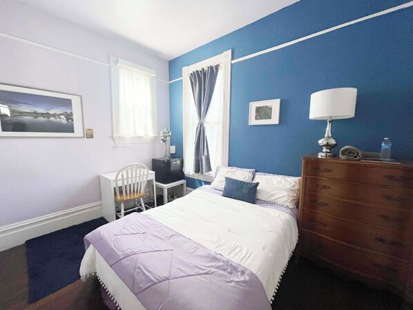 Un dormitorio con cama, escritorio, silla, cómoda y ventana con cortinas.
