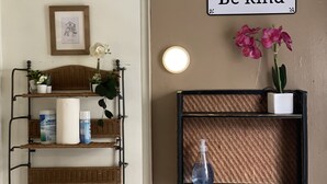 A room with a wicker shelf holding toiletries, a framed picture, and a 'Be kind' sign. - B-Love's Guest House (Oakland)
