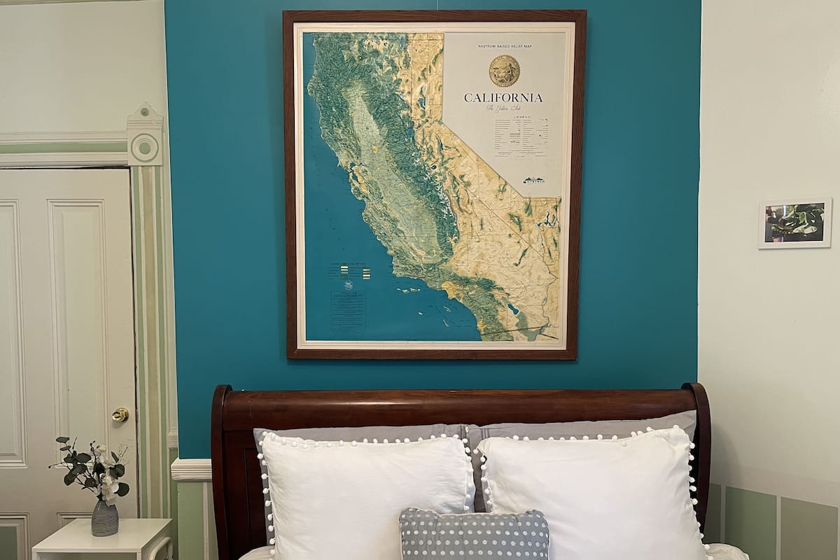 Une chambre à coucher avec un lit, une carte de Californie encadrée et une petite table sur laquelle est posé un vase.