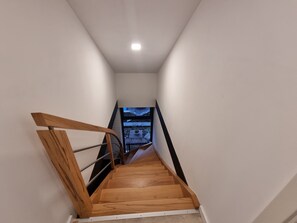 Eine schmale Holztreppe mit Metallgeländer, die zu einer Zwischenebene mit Balkonblick führt.