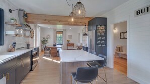 A modern kitchen with a central island, wooden beams, and a dining area with a view of the outdoors.