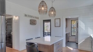 A modern kitchen with a central island, pendant lighting, and a sign reading "BUTTER & EGGS".
