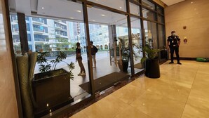 Um saguão de hotel com grandes janelas, uma recepção e um agente de segurança.