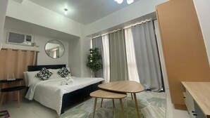 Quarto moderno com cama, mesas de cabeceira, espelho redondo, mesinha e uma janela grande com cortinas.