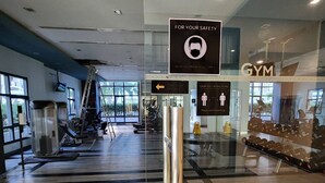 Academia com equipamentos de exercícios, uma placa indicando o uso de máscara facial e uma placa para distanciamento físico.