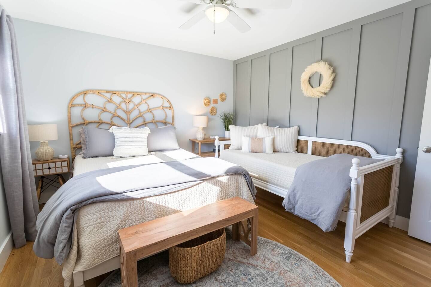 Une chambre avec deux lits, un banc en bois, une table de chevet avec une lampe et une couronne décorative accrochée au mur.