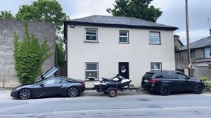 Une maison à deux étages avec un garage, une moto et deux voitures garées devant.