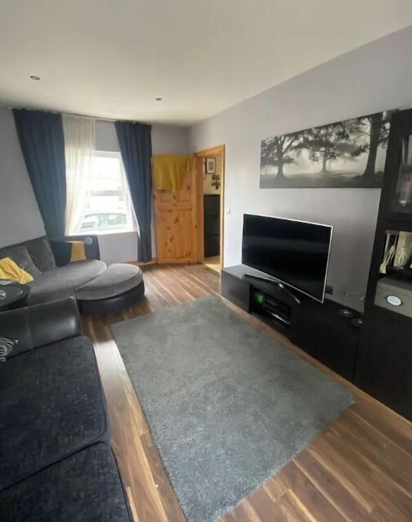 Un salon moderne avec un canapé gris, un téléviseur à écran plat et un plancher en bois.