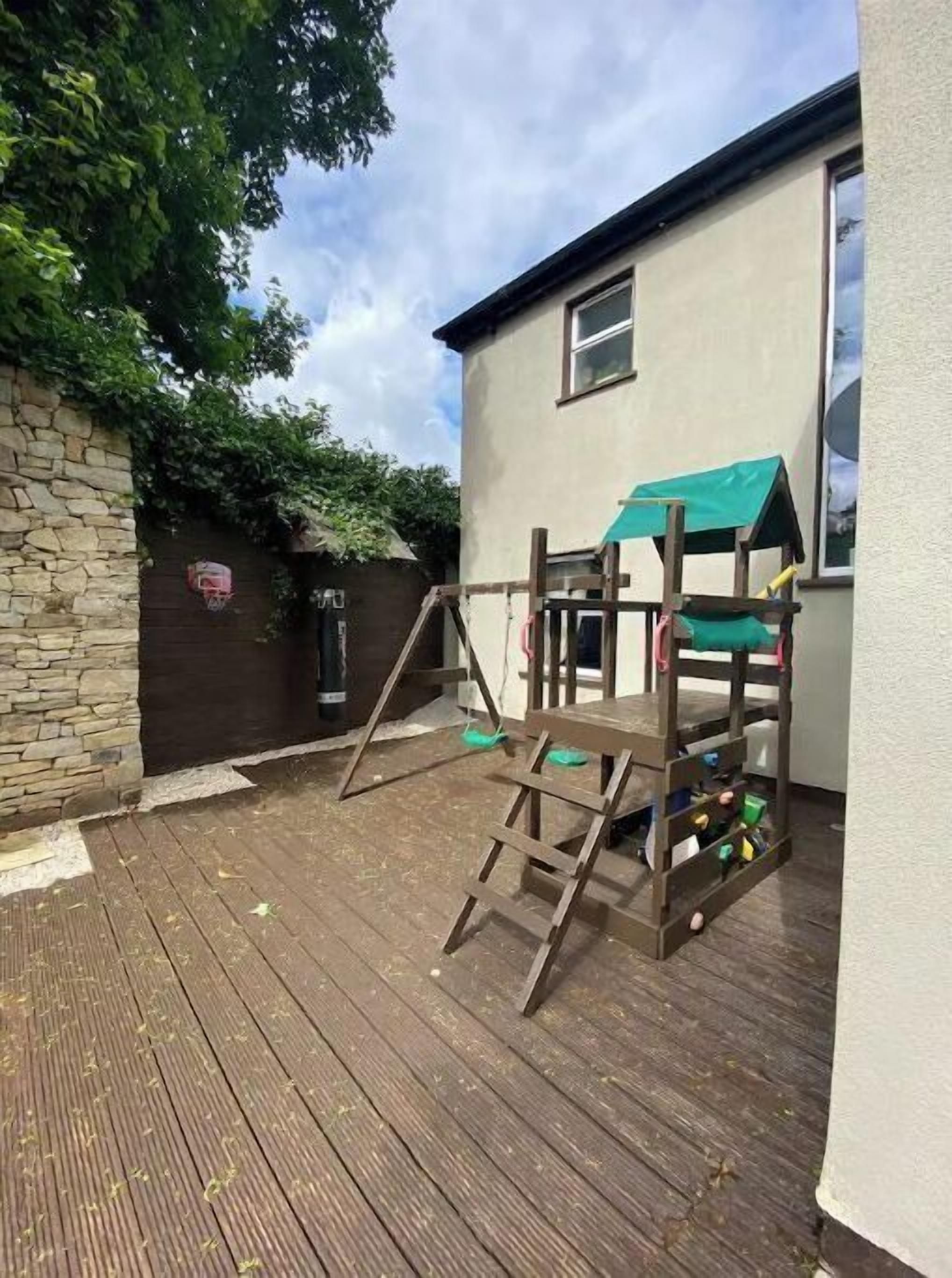 A wooden deck with a play structure, a stone wall, and a house with a green awning.