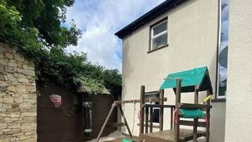 A wooden deck with a play structure, a stone wall, and a house with a green awning.