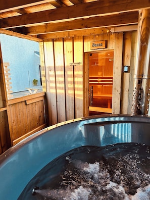 Een houten sauna met een bordje met de tekst 'Sauna' en een grote jacuzzi op de voorgrond.