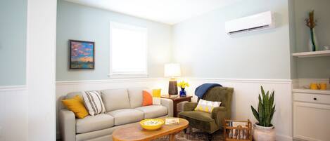A living room with a sofa, armchair, coffee table, and a potted plant.