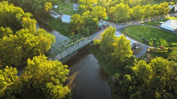 An aerial view of a green bridge over a river, surrounded by lush greenery and residential buildings.