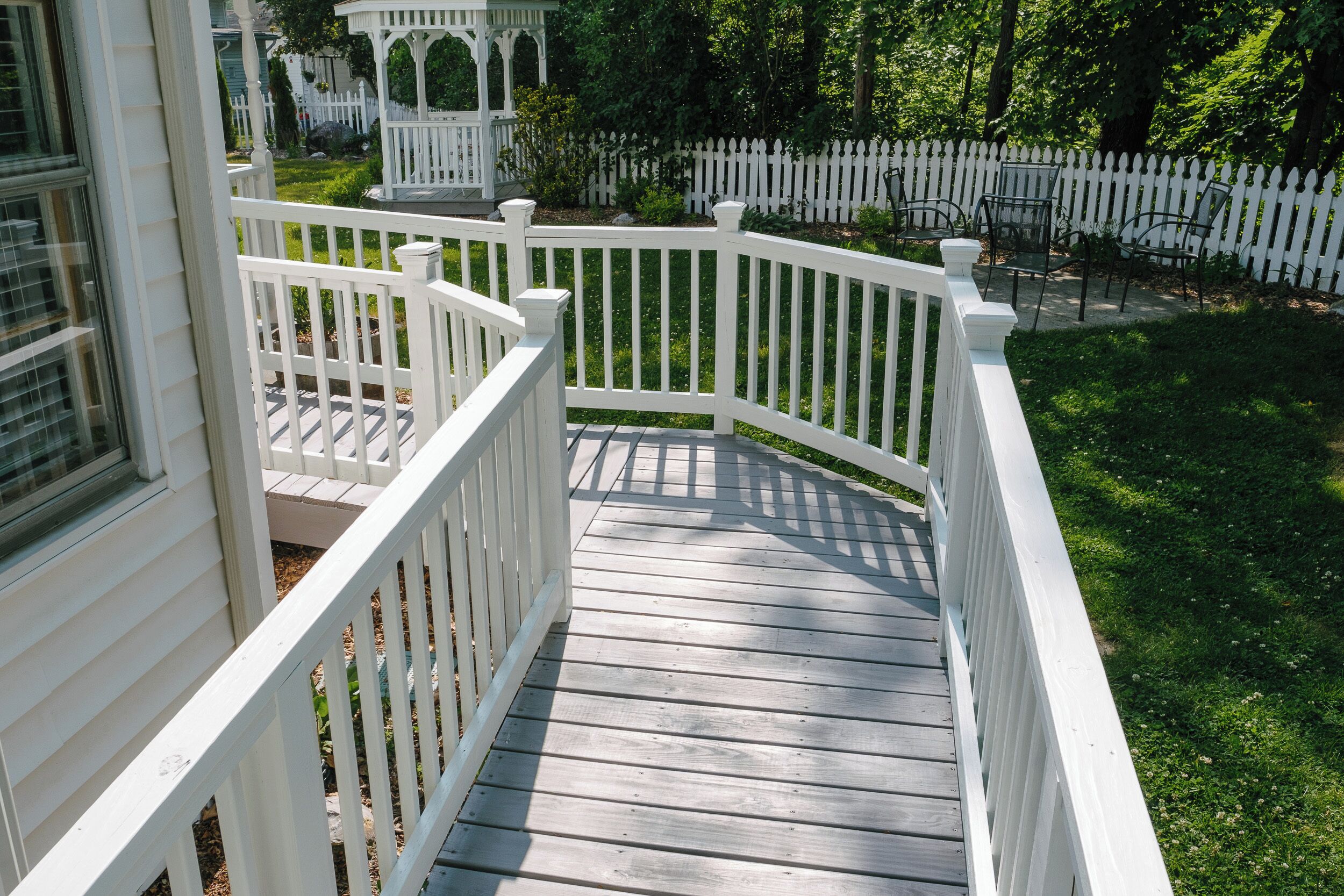 A wooden deck with white railings, a gazebo, and a white picket fence in a garden setting.