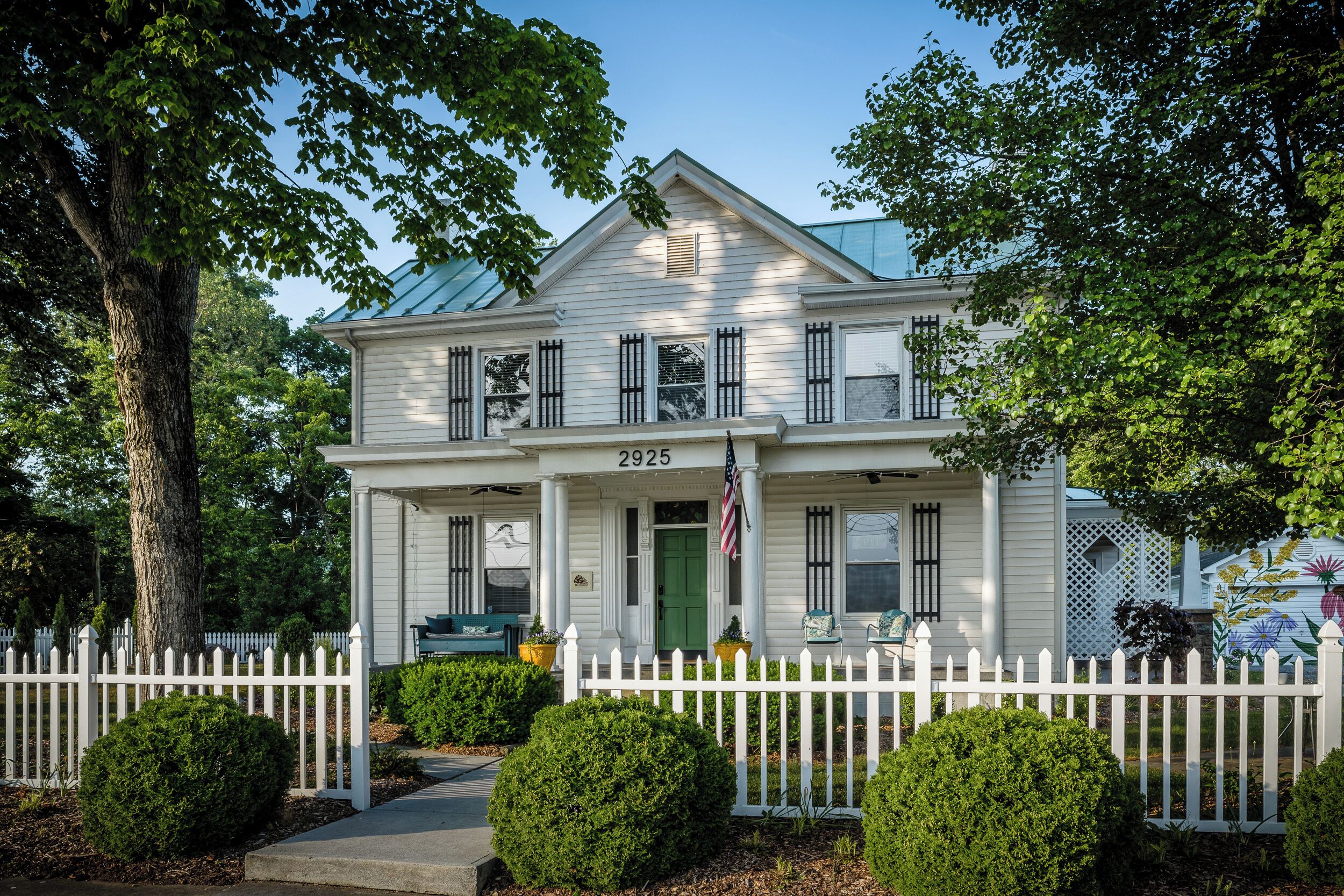 A two-story house with a white picket fence, a green door, and an American flag.