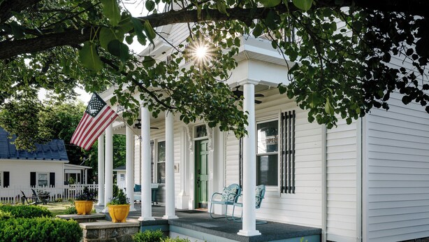 A white house with a porch, a flag, and a bench. - Willow Suite ~ 1 of 5 Unique Stays at Basswood ~ Ground Floor with Ramp Access (Capon Bridge)