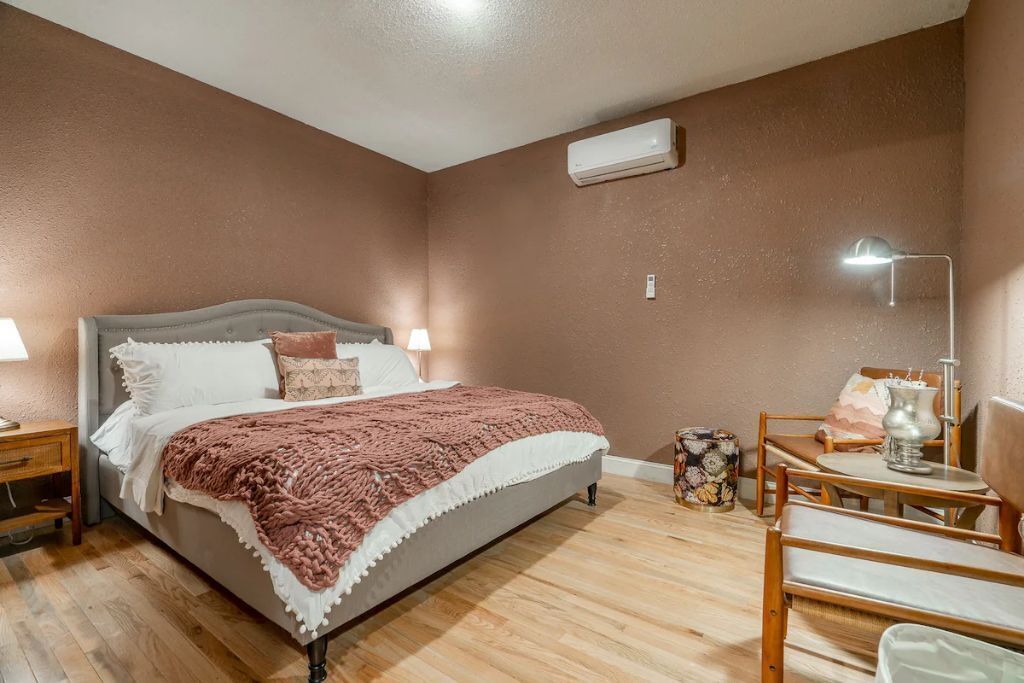 Un dormitorio con cama, mesitas de noche, lámpara, una pequeña mesa con un florero y una silla.
