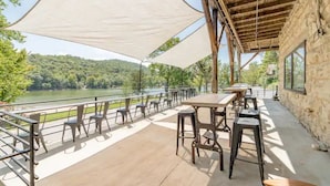 Eine Terrassenanlage im Freien mit Tischen und Stühlen, mit Blick auf einen Fluss und bewaldete Hügel.