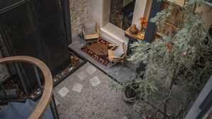 Un patio interior acogedor con suelo de piedra, una silla de madera, una alfombra pequeña y una planta en maceta.