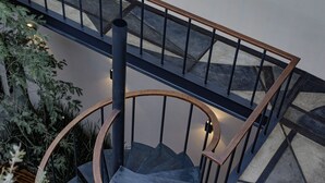 Una escalera de caracol con barandilla de madera y balaustrada de metal negro, rodeada de plantas de interior.