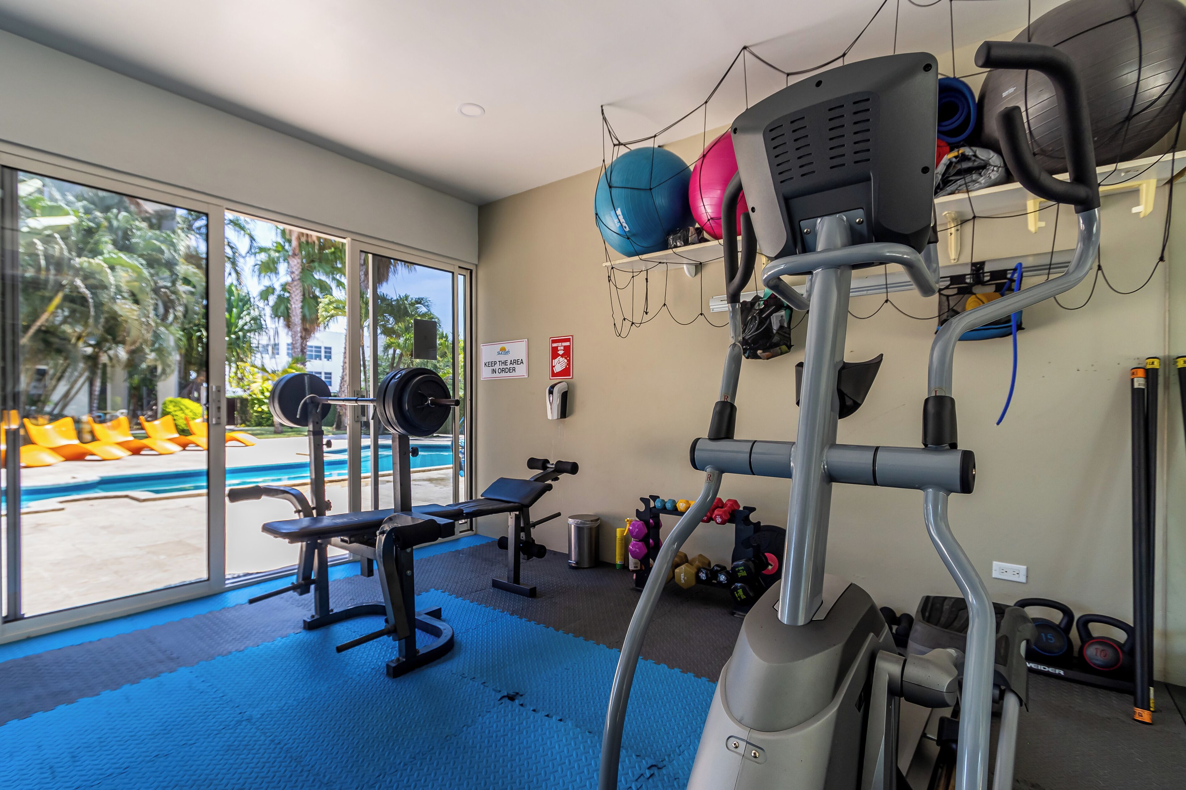 Een fitnessruimte met trainingsapparatuur, een bank en een wandrek met gewichten.