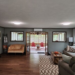 A living room with a wooden floor, a sofa, a red chair, a table, and a door leading to an outdoor patio.