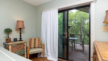 Une pièce avec une porte-fenêtre coulissante donnant sur une terrasse, une petite table avec une lampe, une chaise et une commode ancienne.