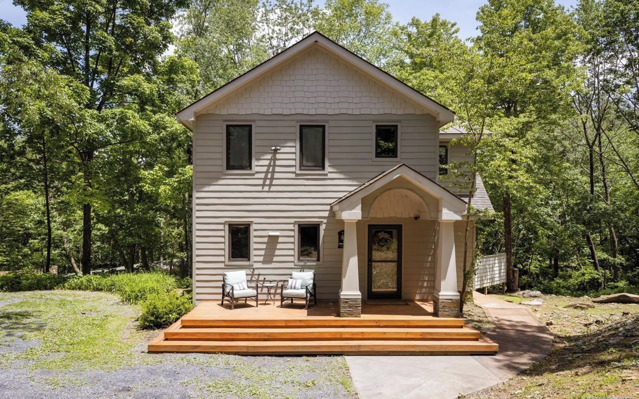 A two-story house with a front porch, a small patio with chairs, and a wooden deck leading to the entrance.