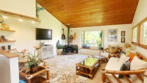 Un salon chaleureux avec un plafond en bois, une cheminée, un téléviseur et des fauteuils confortables.